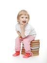 The baby girl is sitting on the pile of books