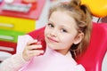 Baby girl sitting in a red dental chair smiling with a red Apple in her hands.