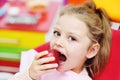 Baby girl sitting in a red dental chair smiling with a red Apple in her hands.