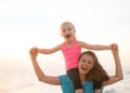 Baby girl sitting on shoulders of mother on beach