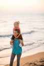 Baby girl sitting on shoulders of mother on beach