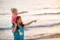 Baby girl sitting on shoulders of mother on beach