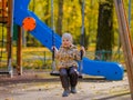 Baby girl sitting on a swing on a playground in an autumn park Royalty Free Stock Photo