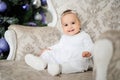 Baby girl is sitting on a vintage armchair in a white room beautiful decorated for christmas holiday with a Christmas tree and Royalty Free Stock Photo