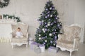 Baby girl is sitting on a vintage armchair in a white room beautiful decorated for christmas holiday with a Christmas tree and Royalty Free Stock Photo