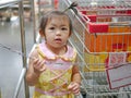 A baby girl is sneakily touching a chain barrier and wants to pass under it at a supermarket - children`s curiosity and