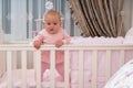 A baby girl standing in crib in pink bedroom scene. Royalty Free Stock Photo