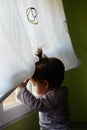 Baby girl on a table lifts a window curtain to peek out of the window