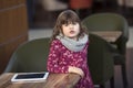 Baby girl with tablet at a table in a cafe, waiting, shopping ce