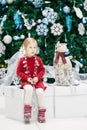 baby girl toddler with blue eyes in red dress sitting by New Year tree near deer toy Royalty Free Stock Photo