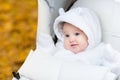 Baby girl in warm white jacket sitting in stroller