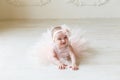 Baby girl wearing a peach tutu. Cute smiling baby girl lying on the floor on creamy background. Adorable smile