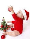 Baby girl wearing a Santa Claus hat, playing with red balls, near the Christmas Tree Royalty Free Stock Photo