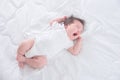 Baby girl wearing white body suit yawning on white bed Royalty Free Stock Photo