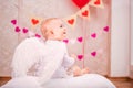 Baby girl with white feather wings sits on white soft pillow among the Valentine`s Day symbol, view from the back Royalty Free Stock Photo