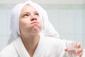 Baby girl, in a white robe and towel on her head, in the bathroom, holding a glass of water and rinsing her mouth, after cleaning
