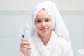 Baby girl, in white robe and towel on her head, in bathroom, holding toothpaste and brush in hand