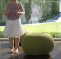 Baby girl with a white skirt standing next to a green footstool