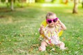 A baby with glasses and a hat on a green lawn in summer in yellow clothes