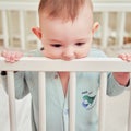 Baby gnaws at the edge crib during teething itching. Funny child scratching his teeth on the rail bed, age six months Royalty Free Stock Photo