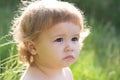 Baby in grass at sunny summer evening. Serious child outdoors. Baby face close up. Funny little child closeup portrait Royalty Free Stock Photo