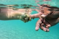 Baby hand holding fathers finger in transparent blue water. Underwater hands of father and small child in clear blue Royalty Free Stock Photo