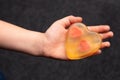 The baby hand holds a handmade yellow soap in the shape of a heart with two hearts inside on a dark background Royalty Free Stock Photo