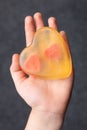 The baby hand holds a handmade yellow soap in the shape of a heart with two hearts inside on a dark background Royalty Free Stock Photo