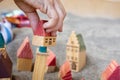 Baby hand with small wooden toy houses on sand. Children game. Five cottages with red roof on grey soil. Modelling