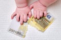 Baby hand and torn money in euros, close-up. Children fingers and an object on a white background