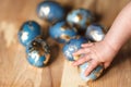 Baby hand touching blue easter eggs decorated gold patel on wood background