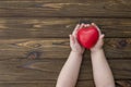 Baby hands holding a red heart against a wood texture background.