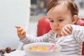 Baby, high chair and playing with bowl for meal, nutrition or healthy porridge with spoon at home. Young adorable cute Royalty Free Stock Photo