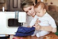 Baby with his mother seamstress, home, natural light, infant curiously looking to sewing machine. Child care and work at Royalty Free Stock Photo