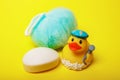 baby hygiene and bath items, baby soap, blue washcloth, yellow duck rubber toy on yellow background