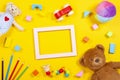 Baby kids toys background with empty frame colorful wooden soft toys and colored pencils on yellow background. Top view Royalty Free Stock Photo