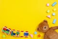 Baby kids toys background with teddy bear, wooden train, colorful blocks and bricks on yellow background. Top view