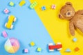 Baby kids toys frame with teddy bear, wooden toy car, colorful bricks on blue and yellow background. Top view Royalty Free Stock Photo