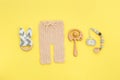 Baby knitted pants, wooden toys and soother on yellow background with copy space