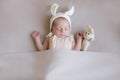 Baby in a knitted rabbit hat with ears and a bunny toy in a beige light blanket. Spring photo. Easter and children.