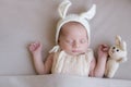 Baby in a knitted rabbit hat with ears and a bunny toy in a beige light blanket. Spring photo. Easter and children.