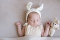 Baby in a knitted rabbit hat with ears and a bunny toy in a beige light blanket. Spring photo. Easter and children.