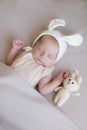 Baby in a knitted rabbit hat with ears and a bunny toy in a beige light blanket. Spring photo. Easter and children.