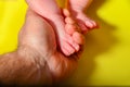 Baby legs on a yellow background, dad holds the small legs of a newborn baby in his hand Royalty Free Stock Photo