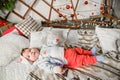 Baby lies on red and white christmas background. Photo of a healthy, chubby baby lying on its back, playing with toes, wearing a