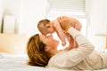 Baby lifted in arms by his mother lying on the bed while playing newly awakened happy