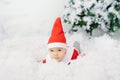 Baby in a little Santa costume lies on artificial snow under a Christmas tree Royalty Free Stock Photo