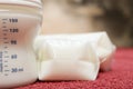 Baby milk in bottle and breastmilk in storage bags on red towel