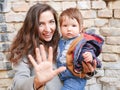 Baby with mom on a brick background. looking at the camera in warm clothes. Happy and young mother sitting on brick background and Royalty Free Stock Photo