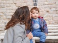 Baby with mom on a brick background. looking at the camera in warm clothes. Happy and young mother sitting on brick background and Royalty Free Stock Photo